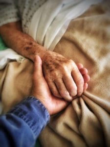 5 Phasen der Trauer: Ein trauernder Sohn hält die Hand seines sterbenden Vaters am Krankenbett